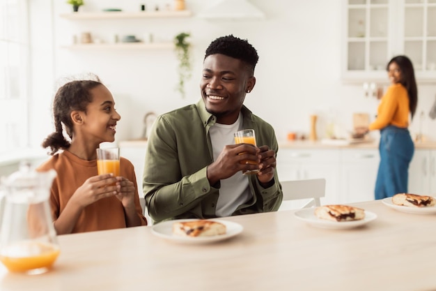 Feliz padre africano e hija bebiendo jugo de naranja en la cocina