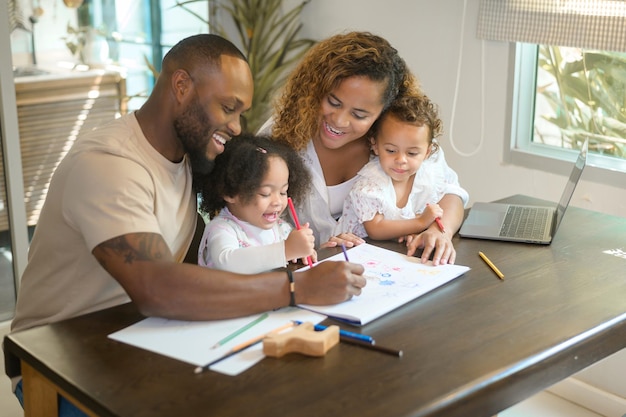 Feliz padre afroamericano jugando y dibujando con sus hijas en casa