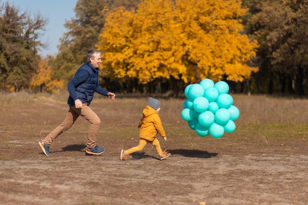 Feliz padre disfruta de pasar el día libre con su hijo en el parque de otoño. Jugar con globos