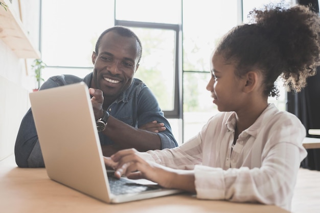 Feliz padre e hija afroamericanos sentados en un café con una laptop