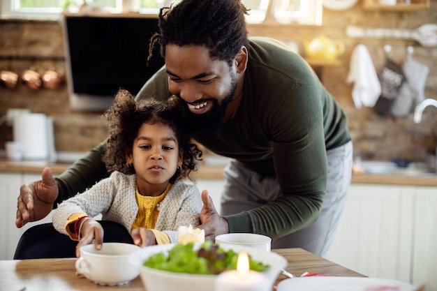 Feliz padre e hija afroamericanos sirviendo comida en la mesa de comedor