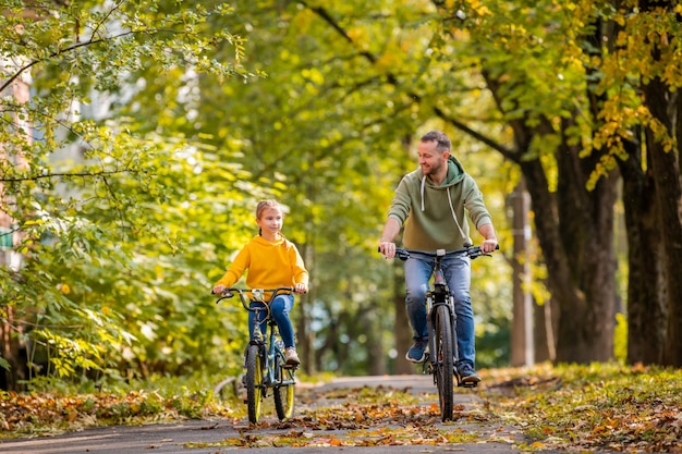 Feliz padre e hija andan en bicicleta en el parque de otoño en un día soleado