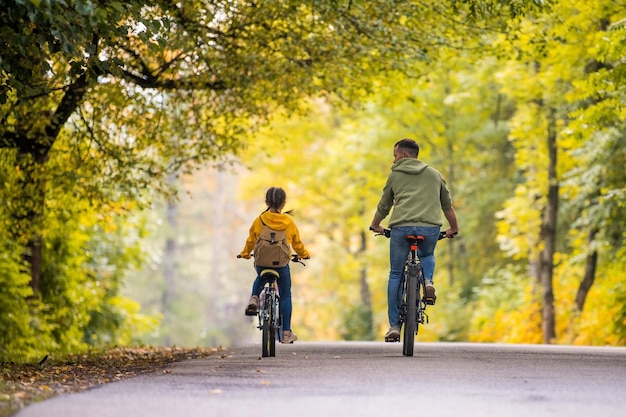 Feliz padre e hija andan en bicicleta en el parque de otoño en un día soleado