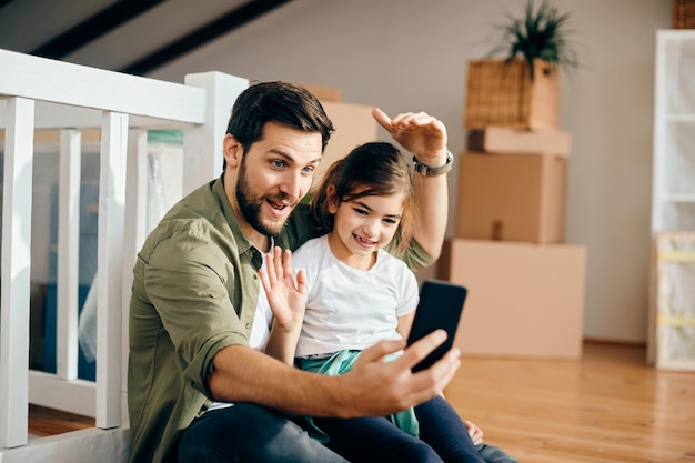 Feliz padre e hija haciendo videollamadas por teléfono inteligente en su nuevo hogar