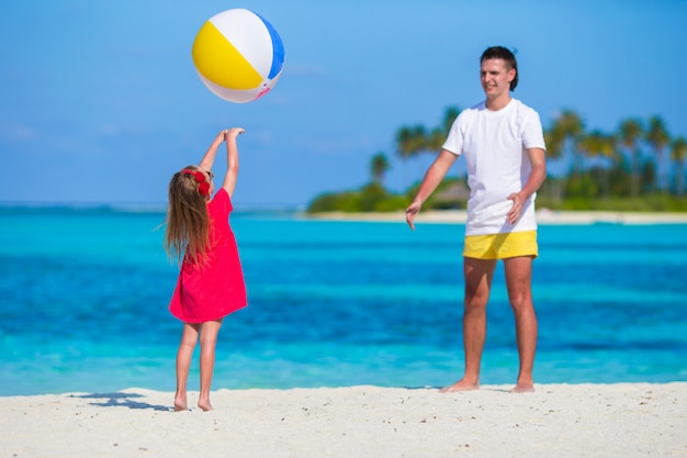 Feliz padre e hija jugando con pelota divirtiéndose al aire libre en la playa