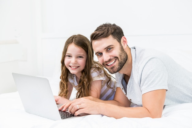 Feliz padre e hija usando laptop en la cama