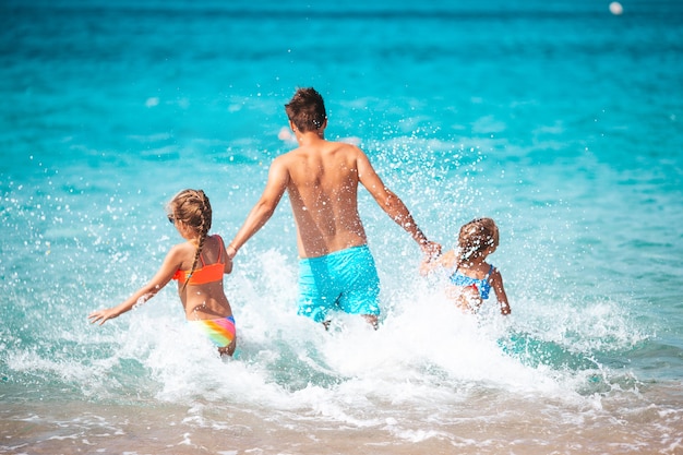 Feliz padre e hijas pequeñas en vacaciones en la playa juegan en aguas poco profundas