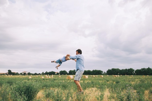 Feliz padre e hijo Antecedentes familiares Papá y su pequeño y lindo niño jugando y abrazándose en el campo de trigo con montones de heno en el día de verano en la naturaleza al aire libre