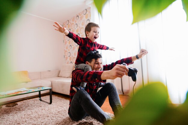 Foto feliz padre e hijo celebrando ganar el primer lugar en un videojuego. hijo está sentado sobre la espalda del padre con los brazos levantados.