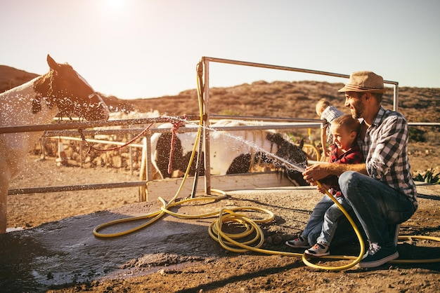 Feliz padre e hijo lavando su caballo en el rancho Centrarse en las caras de los niños