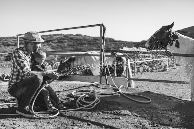 Feliz padre e hijo lavando su caballo en el rancho de la granja