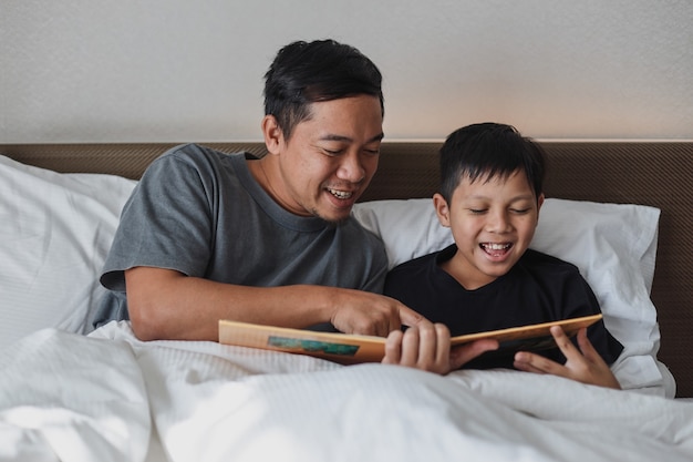 Feliz padre e hijo leyendo un libro juntos en la cama