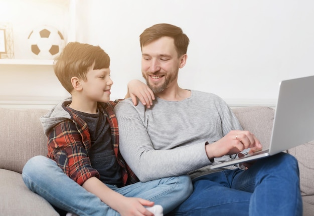 Feliz padre e hijo pasan tiempo juntos y usan la computadora portátil mientras están sentados en el sofá en casa