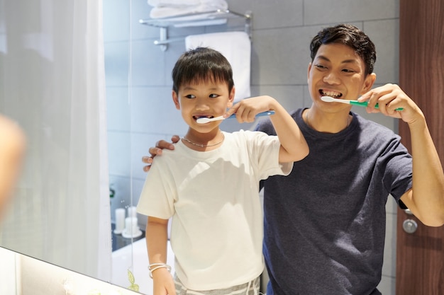 Feliz padre e hijo vietnamita cepillarse los dientes delante del espejo del baño por la mañana