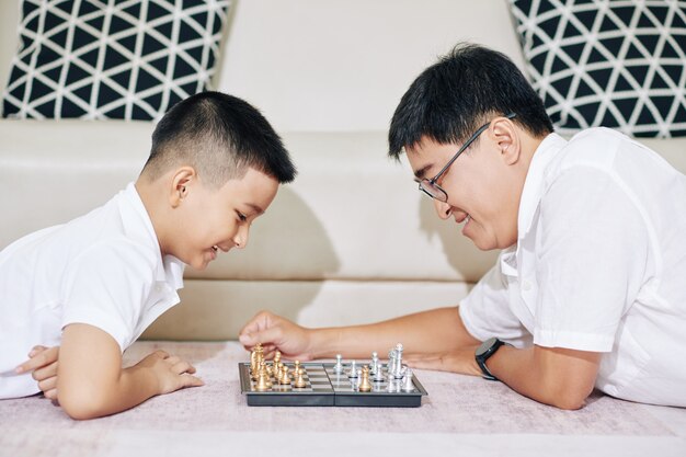 Feliz padre e hijo vietnamitas acostado en el sofá y jugando al ajedrez