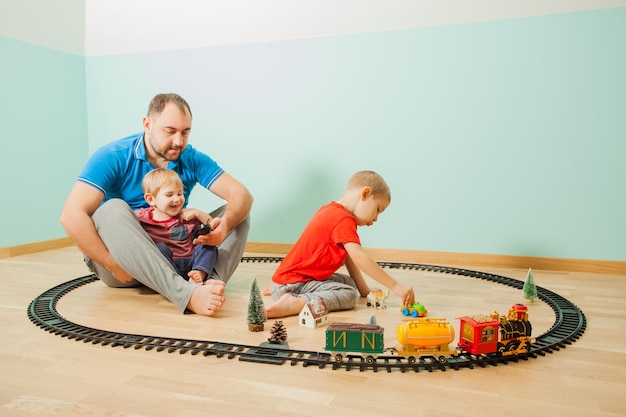 Feliz padre e hijos juegan un tren de juguete en la sala de juegos