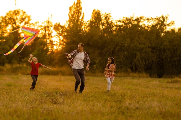 feliz padre de familia e hija corren con una cometa en la pradera