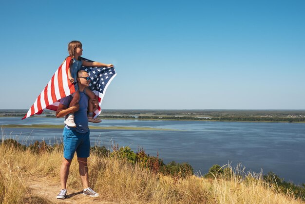 Feliz padre de familia e hijo con la bandera de los Estados Unidos de América disfrutando del atardecer en la naturaleza