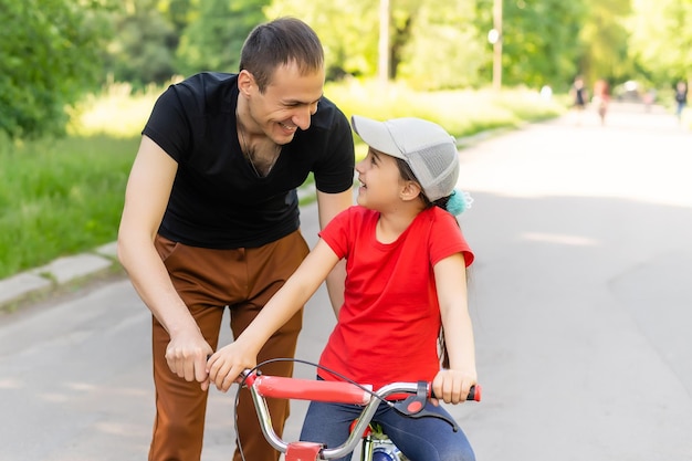 feliz padre de familia enseña a su hija a andar en bicicleta en el parque en la naturaleza.