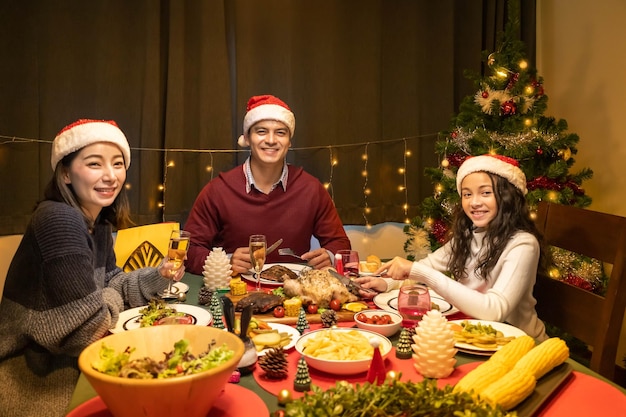 Feliz padre de familia madre e hija cenando juntos para celebrar las vacaciones de Navidad juntos mirando a la cámara