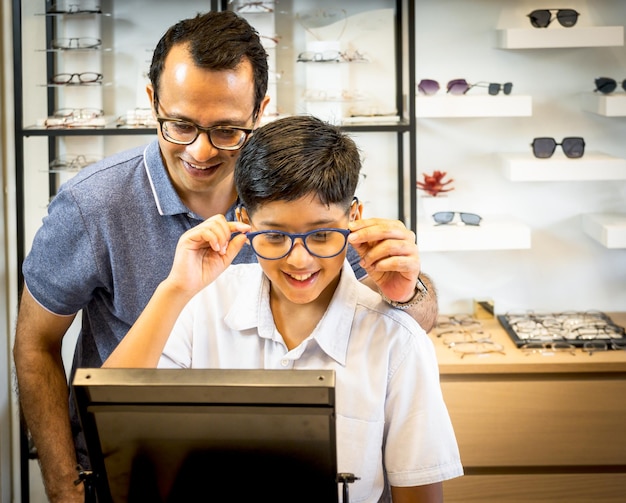 Feliz padre indio y lindo hijo eligiendo anteojos en una tienda de ópticaxA