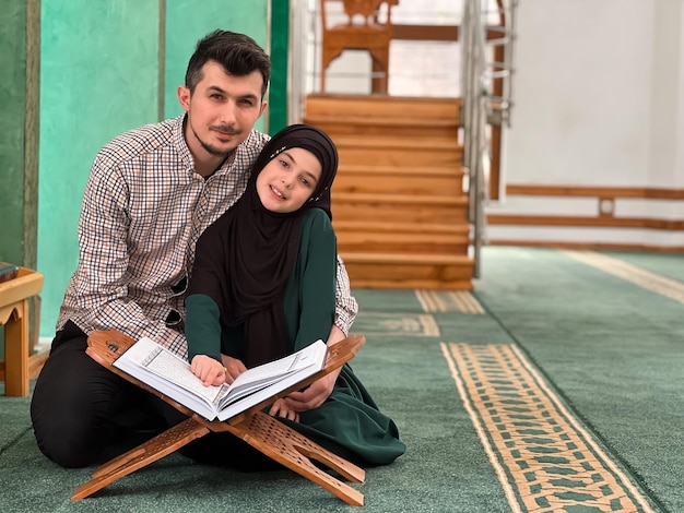 Un feliz padre joven de familia musulmana con una hija leyendo un Corán dentro de la mezquita