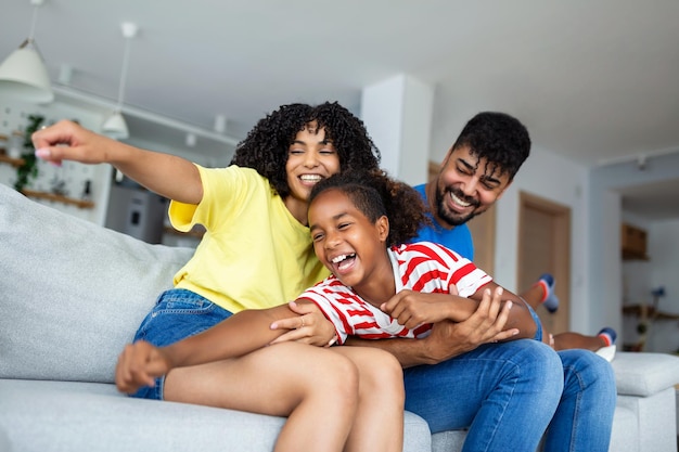 Feliz padre y madre afroamericanos que llevan a cuestas a una hija orgullosa y emocionada que juega a un superhéroe volador que alcanza el brazo hacia adelante Una niña alegre monta a sus padres de vuelta jugando un juego activo con la familia en casa