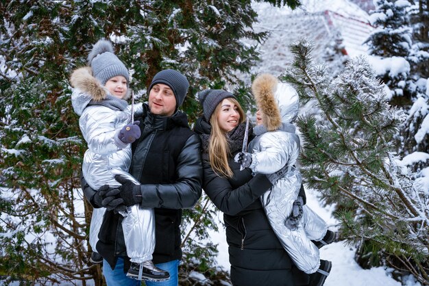 Feliz padre y madre sostienen a los niños, hijo e hija en sus brazos en un día nevado de invierno en la nieve ...