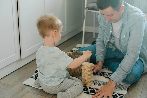 Feliz padre y niño pequeño niño pequeño hijo jugando con bloques de madera en la habitación de los niños en casa