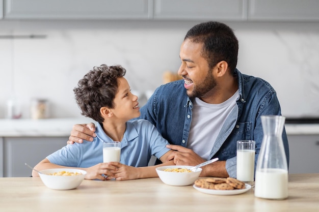 Un feliz padre y su hijo afroamericanos desayunan juntos.