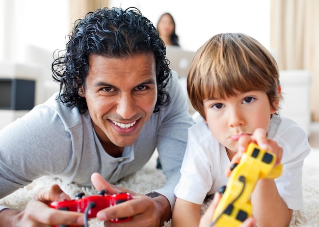 Foto feliz padre y su hijo jugando videojuegos tirado en el piso