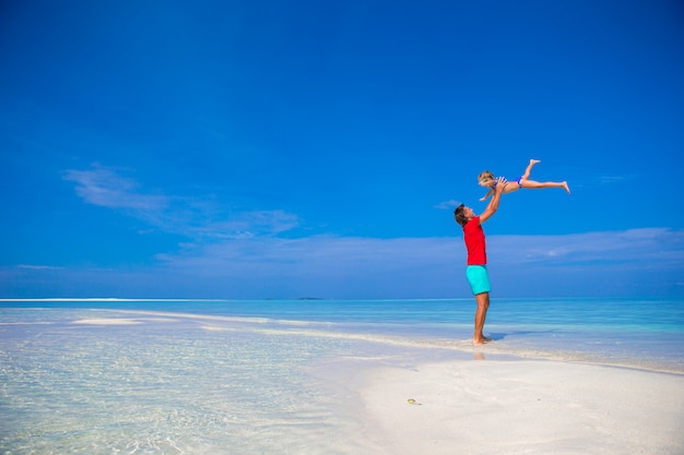 Feliz padre y su pequeña hija adorable en playa tropical divirtiéndose