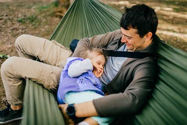 feliz padre y su pequeña hija descansando en una hamaca en la naturaleza