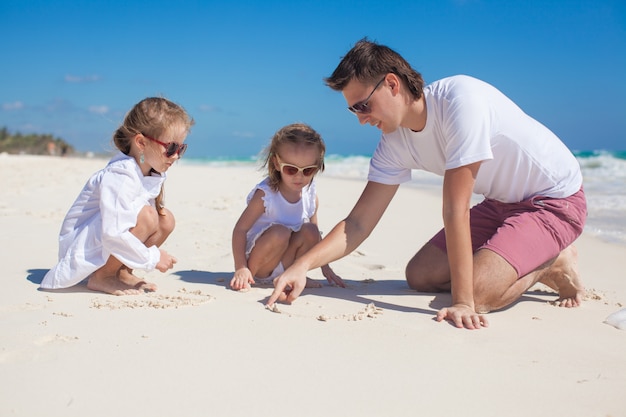 Feliz padre y sus adorables hijas jugando en la playa