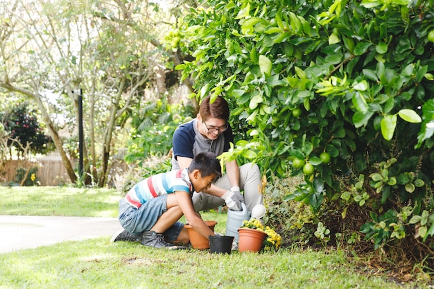 Feliz pai asiático e filho sorrindo, usando luvas e plantando plantas juntos no jardim. tempo de lazer familiar na jardinagem doméstica.