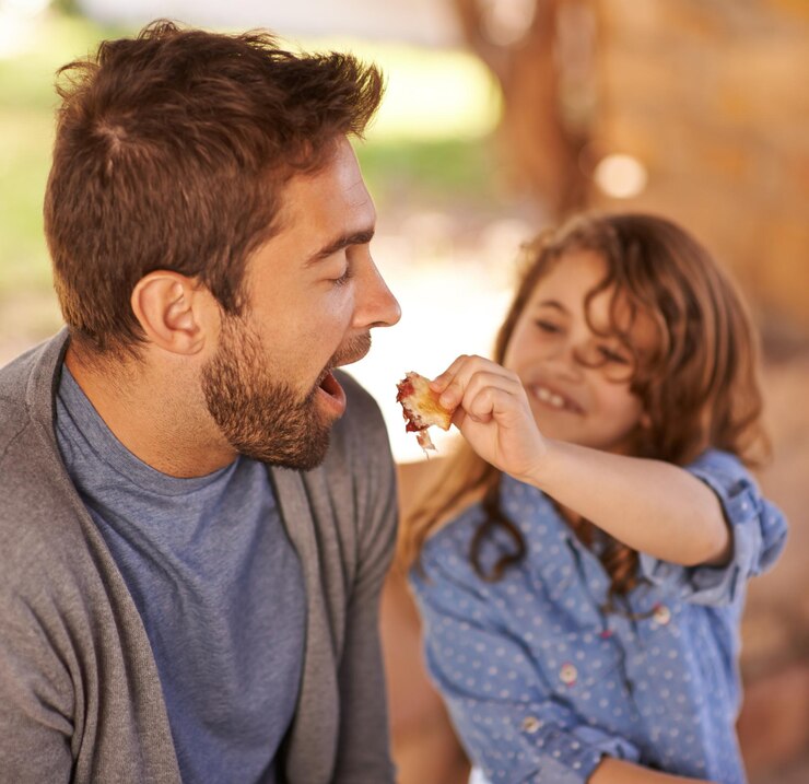 Foto feliz pai comida e menina alimentação de manhã no banco com a família para o pequeno-almoço nutrição e felicidade pai criança e refeição ao ar livre para a saúde da comida e compartilhamento com a boca aberta sorriso e alegria