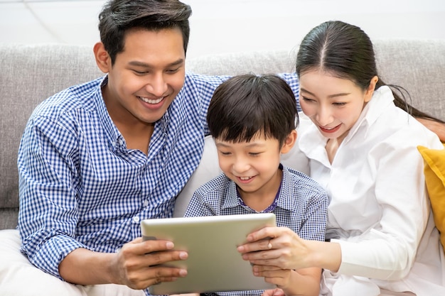 Feliz pai da família asiática mãe e filho sentados no sofá usando tablet juntos na sala de estar