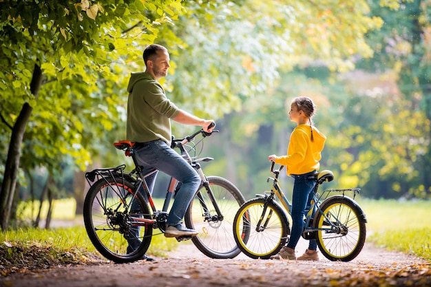 Feliz pai e filha andam com bicicletas no parque outono em um dia ensolarado