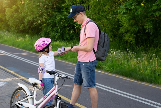 feliz pai e filha andam de bicicleta no parque de verão ajudam a proteger a segurança