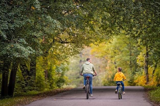 Feliz pai e filha andam de bicicleta no parque outono em dia ensolarado