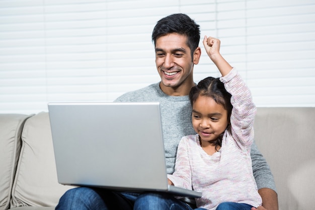 Feliz pai e filha usando o laptop no sofá