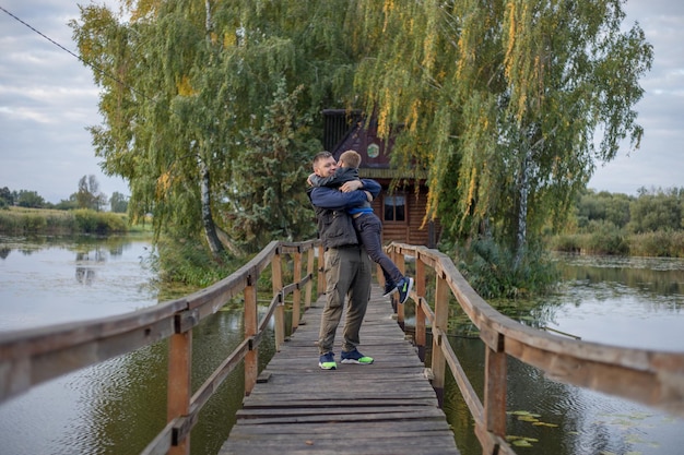 Feliz pai e filho abraçando e brincando juntos na natureza verde Casa do pescador com uma ponte de pedestres de madeira em uma pequena ilha no meio do lago