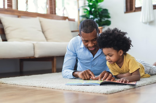 Feliz pai e filho afro-americanos estão lendo um livro e sorrindo enquanto estão deitados no chão, passando um tempo juntos em casa Conceito de educação e desenvolvimento infantil