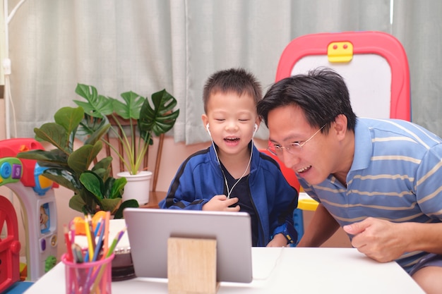 Feliz pai e filho asiáticos com um tablet fazendo videochamada para a mãe ou parentes em casa