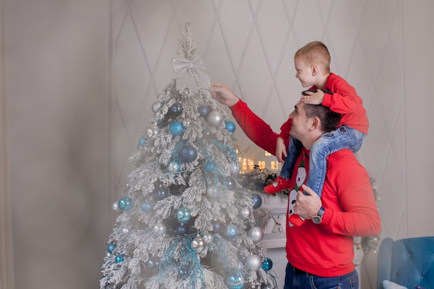 Feliz pai e filho desfrutando de decorar a árvore de Natal com bolas de Natal e guirlanda de luz se preparando para comemorar as férias de inverno: Feliz Natal e Feliz Ano Novo 2021. Conceito de família.