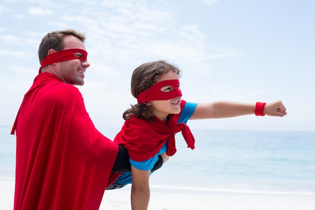 Foto feliz pai e filho em traje de super-heróis, desfrutando na praia