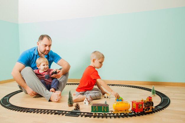 Feliz pai e filhos jogam uma ferrovia de brinquedo na sala de jogos