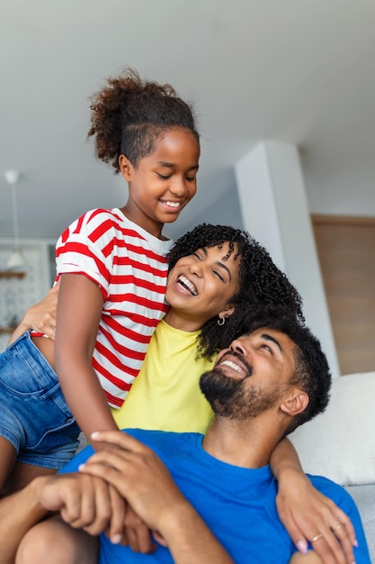 Foto feliz pai e mãe com sua filha fofa abraçam e se divertem sentados no sofá na sala de estar em casa