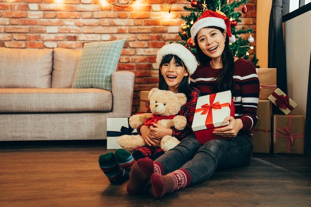 Feliz pai e menina segurando presentes de natal no dia do boxe sentado no chão usando meias coloridas encaram a câmera sorrindo alegremente. árvore de natal decorada no fundo da casa quente.