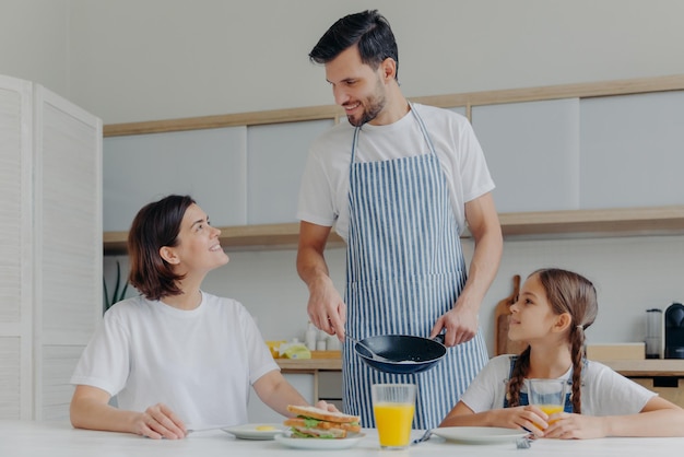 Feliz pai mãe e filha se reúnem na cozinha comem delicioso café da manhã papai preparou ovos fritos estando de bom humor pronto para começar um novo dia família adorável desfruta de uma refeição saborosa em casa